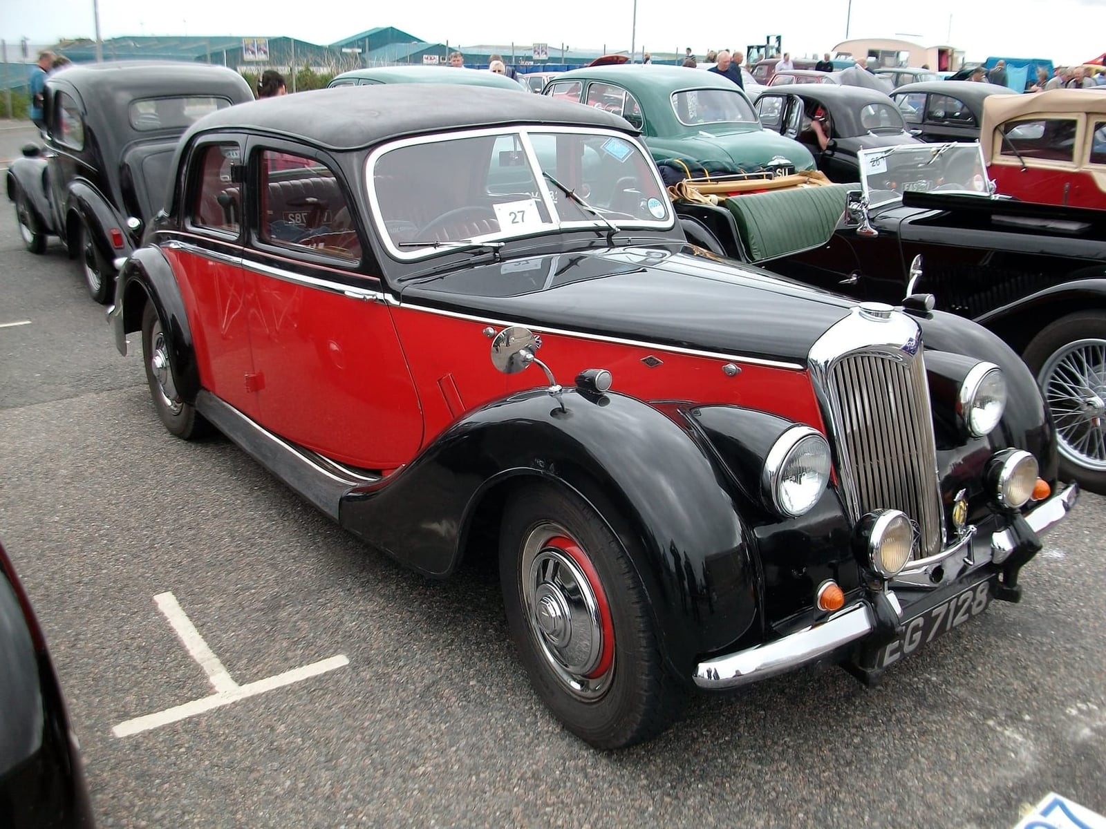 A red and black Riley RMF saloon parked on tarmac at a classic car event, front three-quarter view