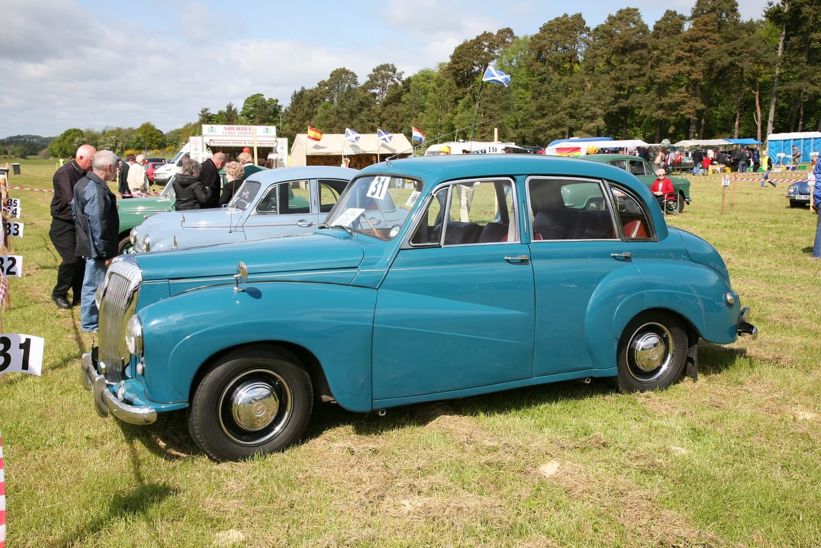 A pale blue Daimler Conquest saloon on grass at a classic vehicle rally, front three-quarter view