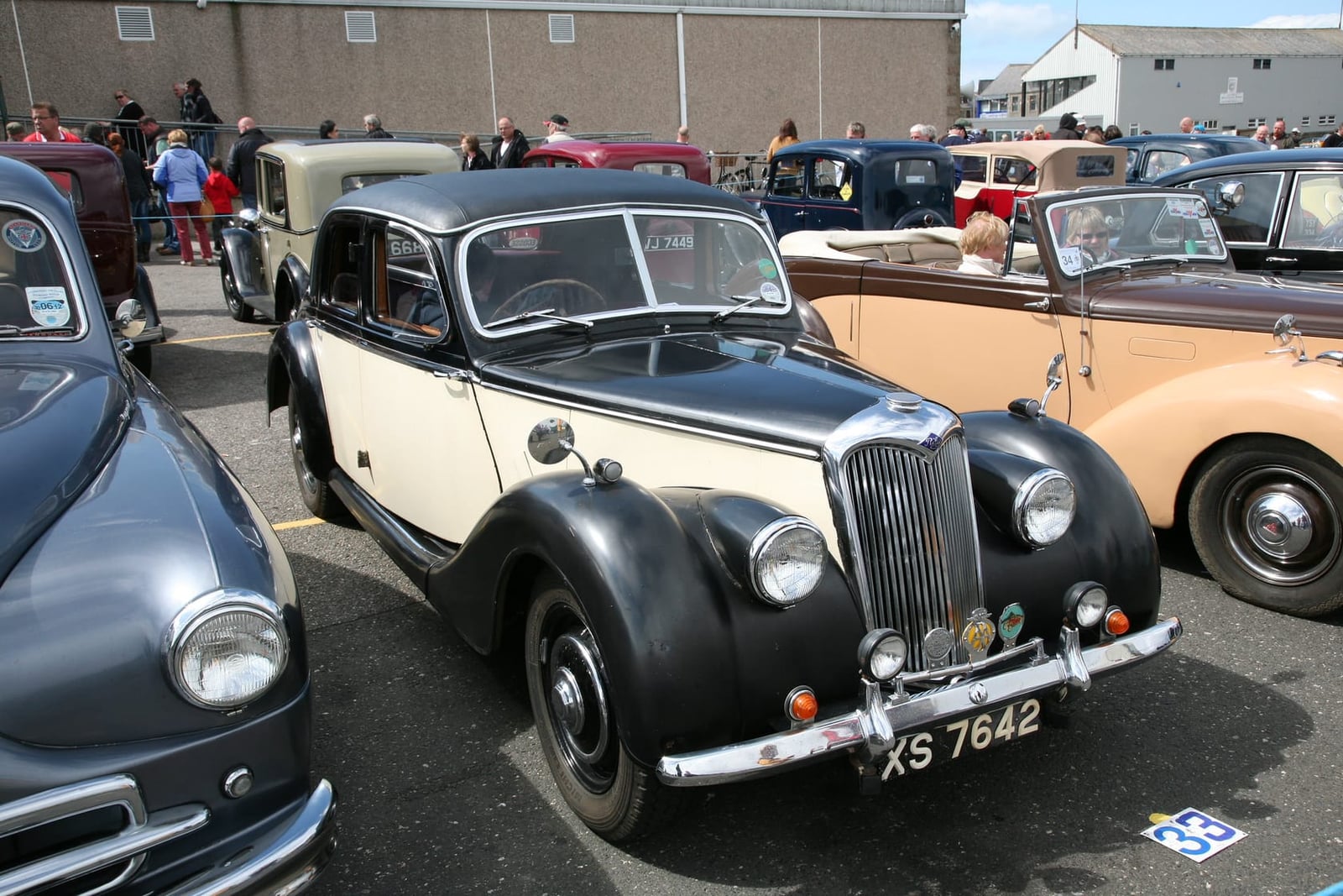 A cream and black Riley RMA saloon at a classic vehicle gathering, front three-quarter view, UK registration XS 7642