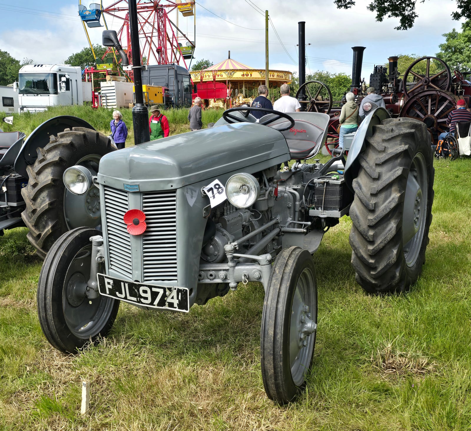 A grey Ferguson TE-20 at a vintage steam rally, fairground rides behind