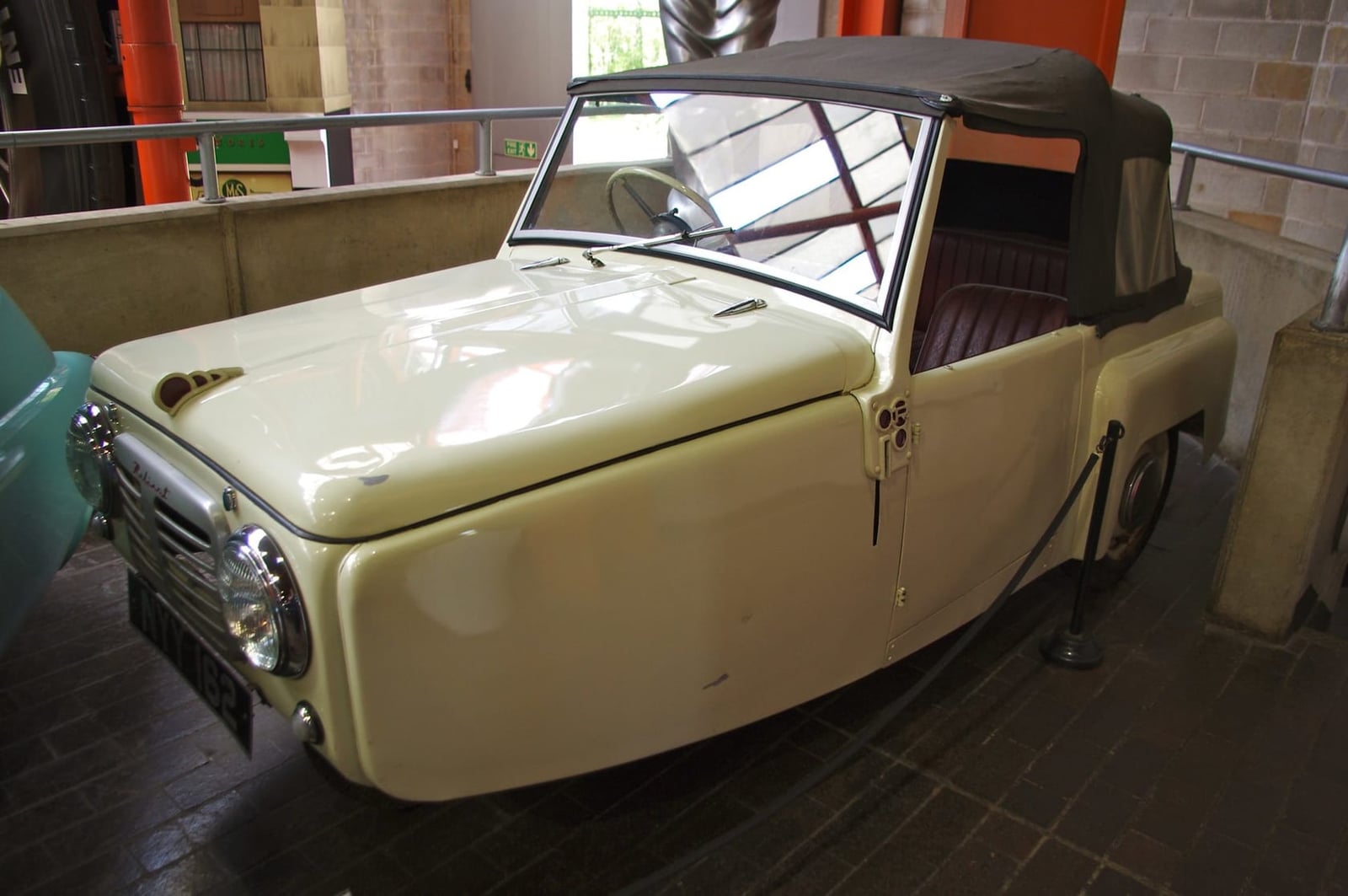A cream 1953 Reliant Regal Mk 1 with its soft top raised, displayed in a museum