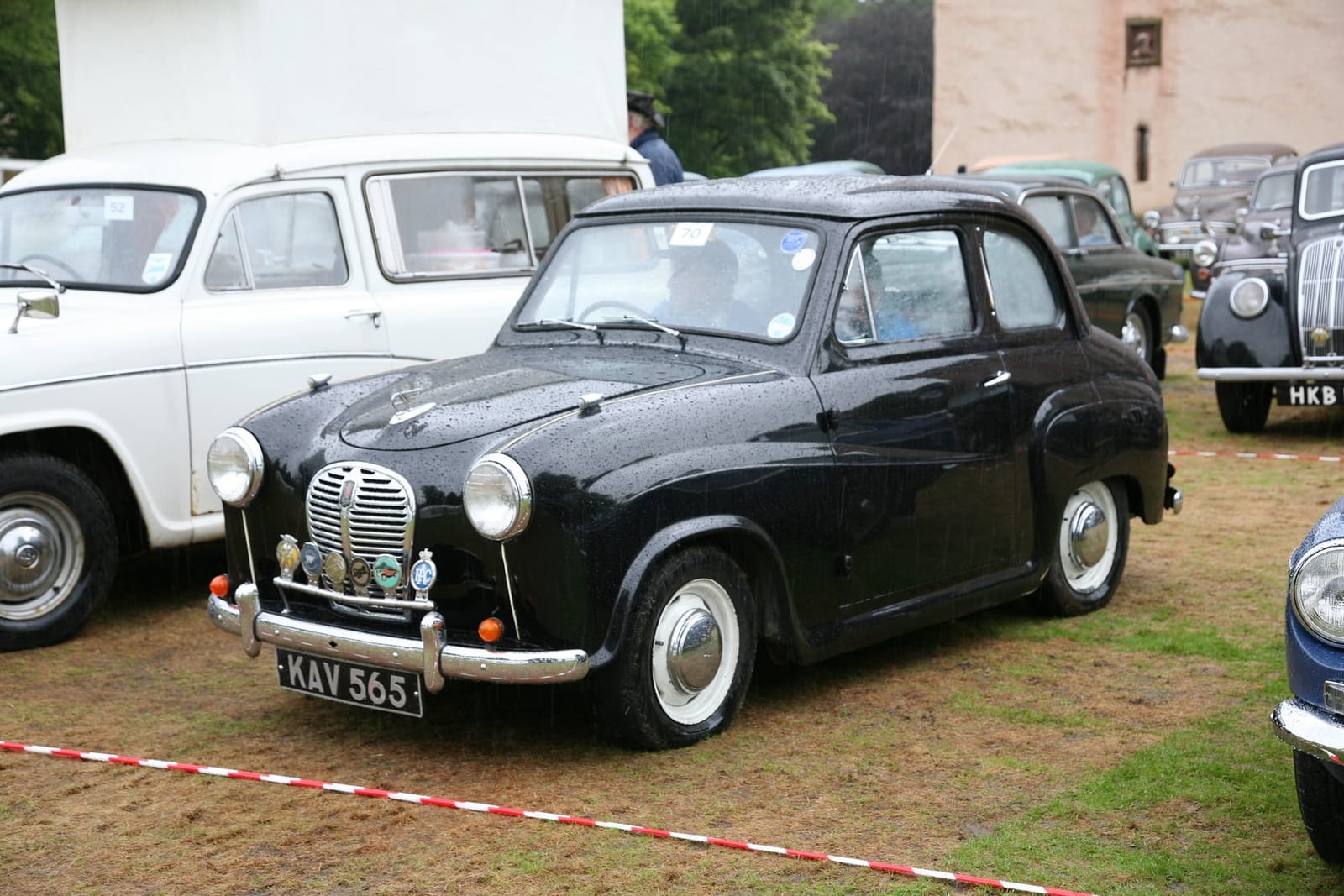 A black 1954 Austin A30 parked on grass at a classic vehicle rally, front three-quarter view