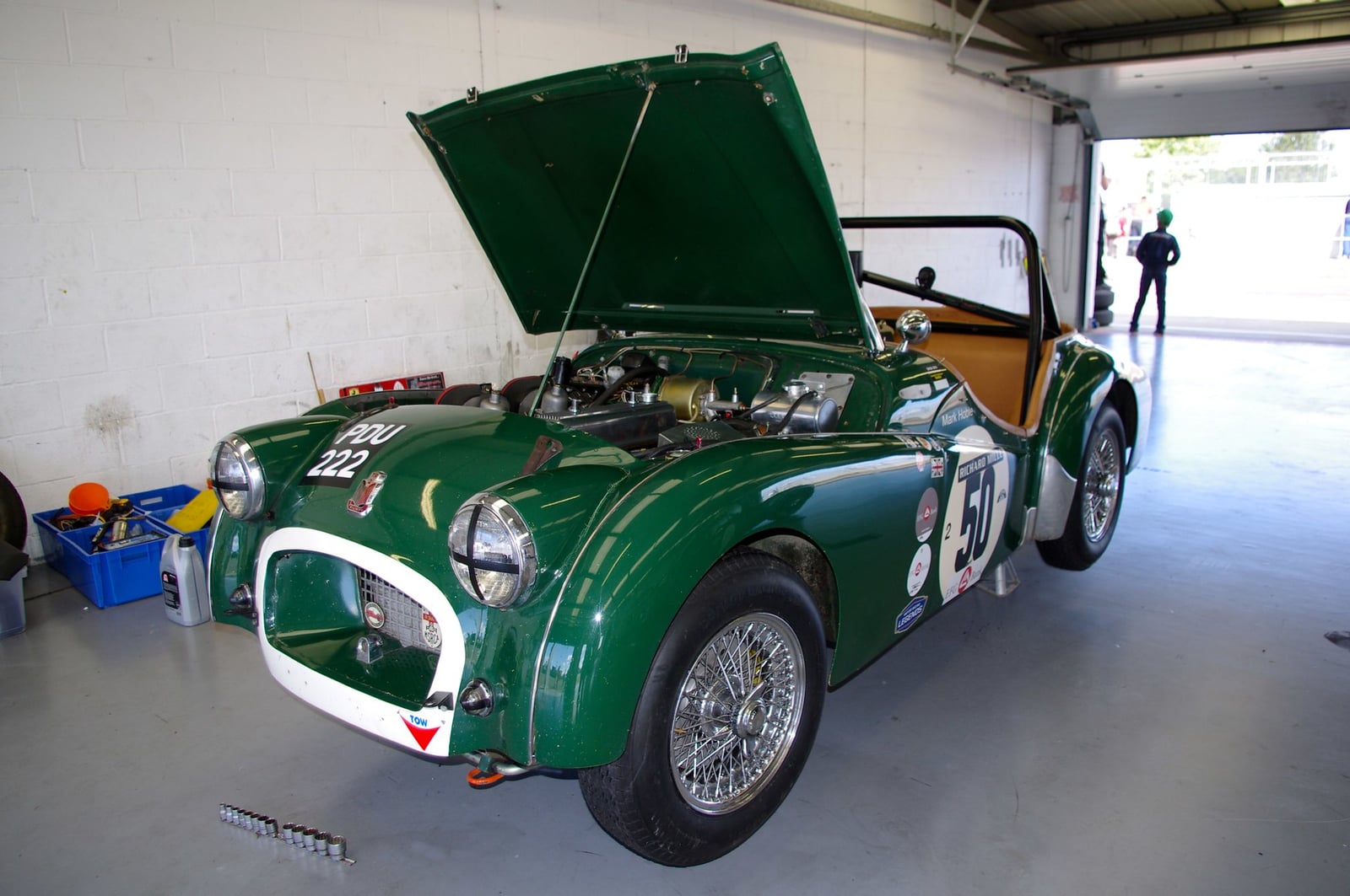 A green Triumph TR2 with the bonnet raised in a garage, showing the four-cylinder engine