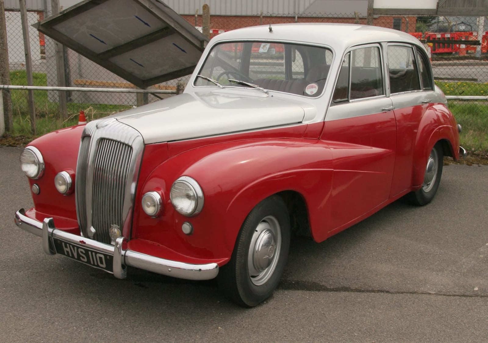 A red and cream 1955 Daimler Conquest saloon at an indoor classic car show, front three-quarter view, UK registration YVS 110