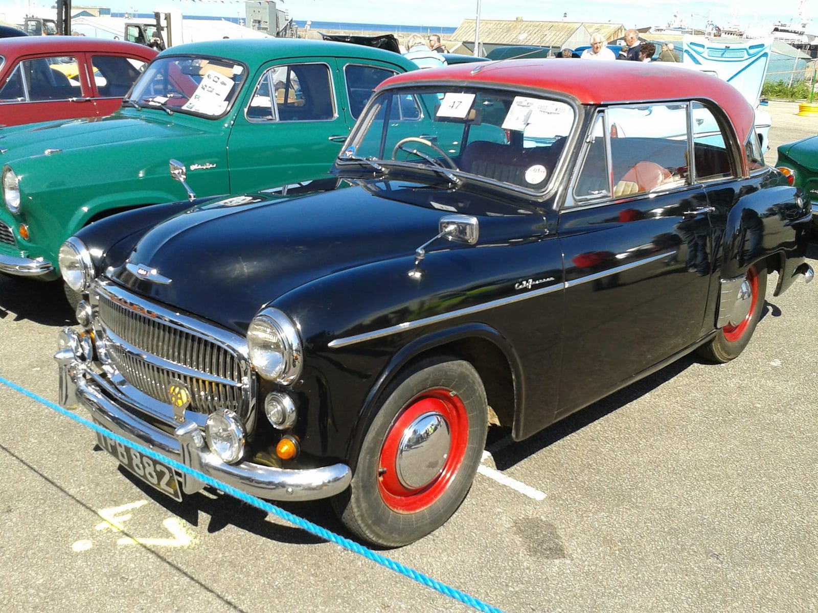 A black and red 1955 Hillman Minx Mk 8 Californian at a show, side view