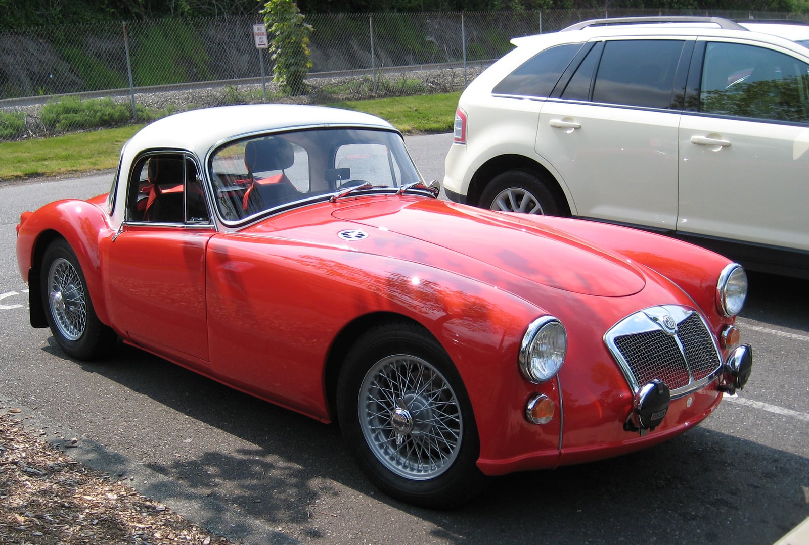 A red MG MGA roadster with a white hardtop, front three-quarter view on a street
