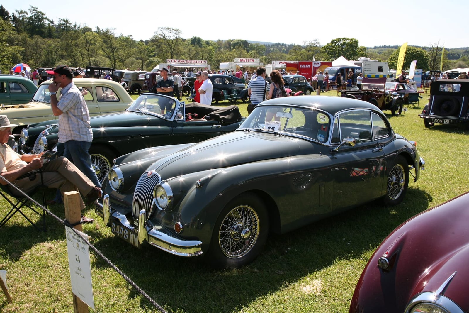A dark green 1960 Jaguar XK150 fixed head coupe on a showfield, front three-quarter view