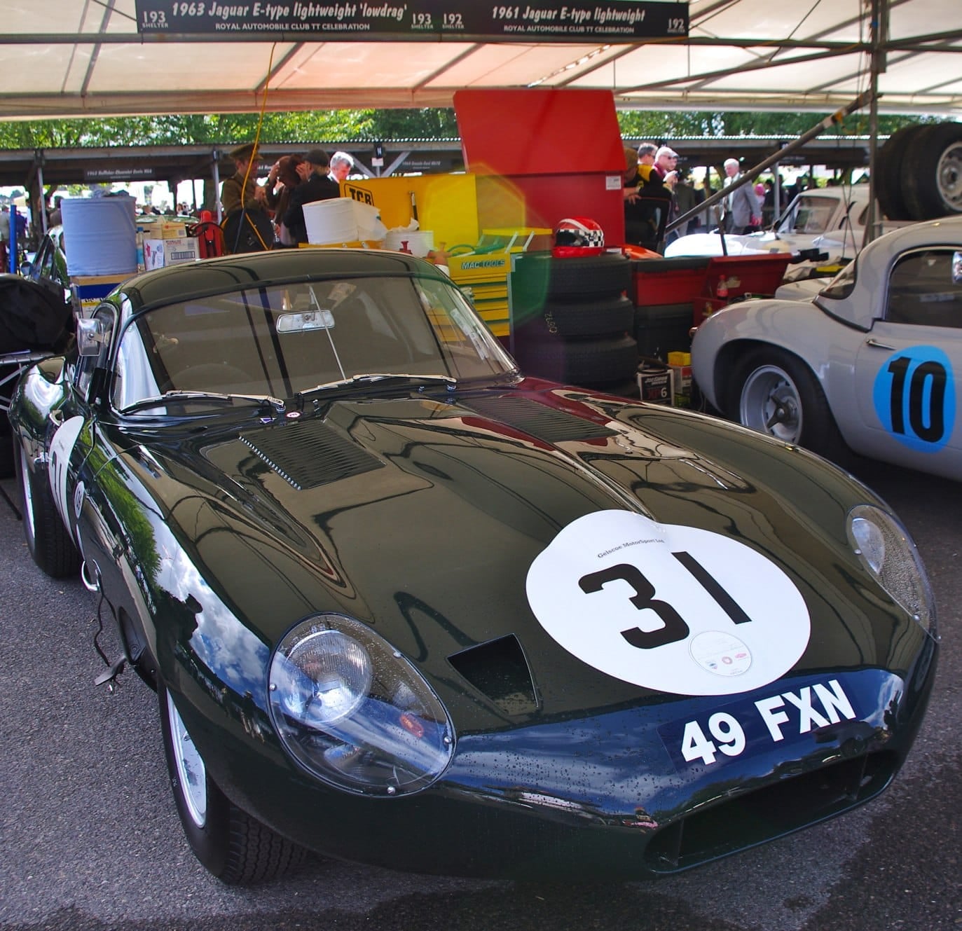 A dark green 1963 Jaguar E-Type Lightweight low-drag coupé wearing race number 31 in the paddock at Goodwood
