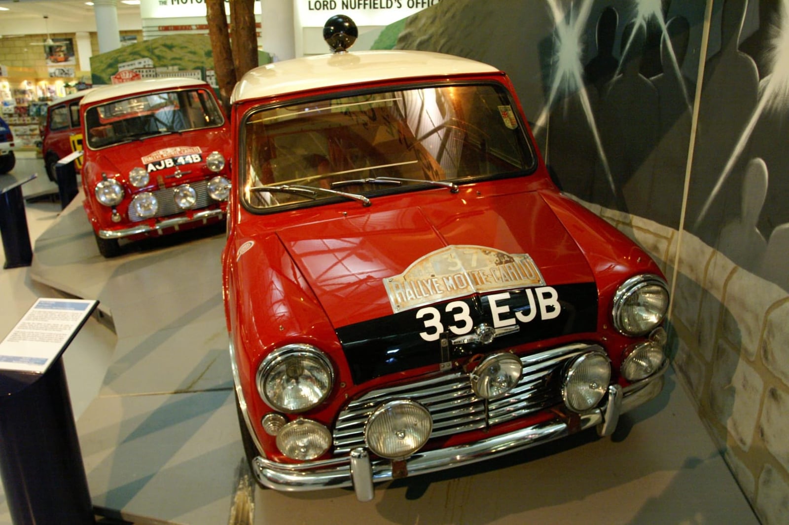 The red 1963 Morris Mini Cooper S that won the 1964 Monte Carlo Rally, registration 33 EJB, displayed in a museum with a sister works car behind