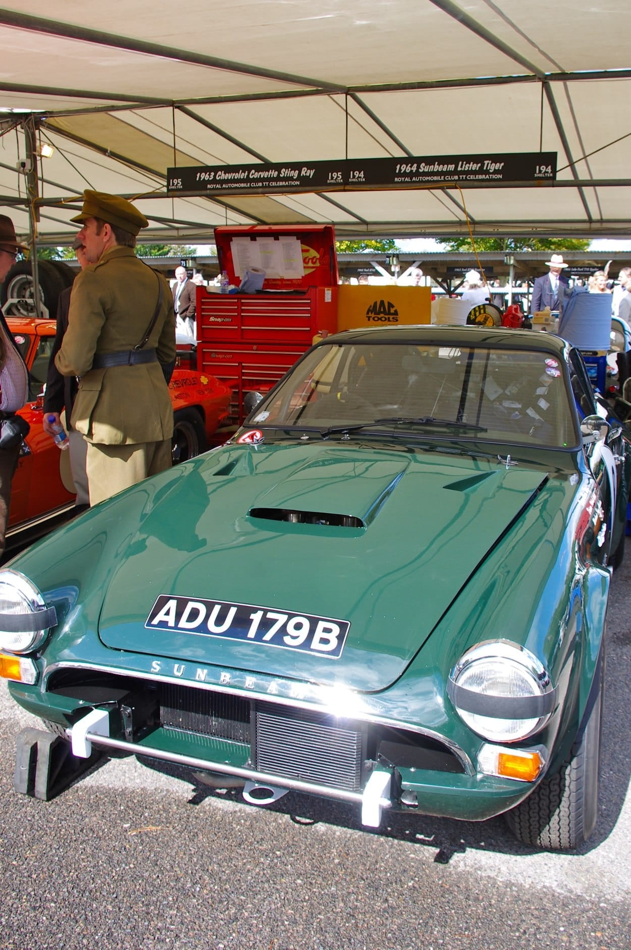 A green 1964 Sunbeam Lister Tiger competition car on indoor display, front three-quarter view, UK registration ADU 179B