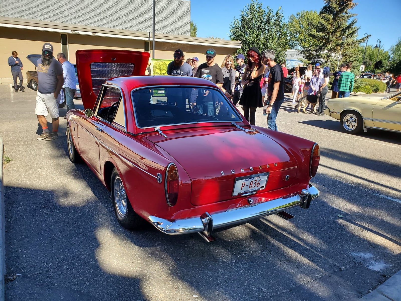 A red 1964 Sunbeam Tiger Mk I with hardtop at a North American car gathering, rear three-quarter view