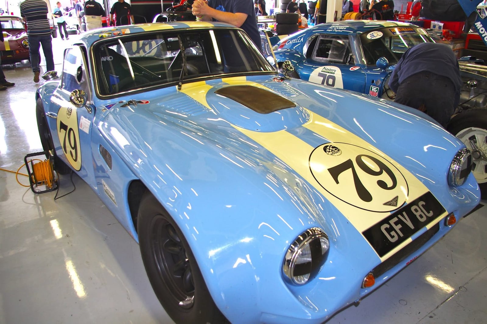 A light blue 1965 TVR Griffith racing car with number 79 and UK registration GFY 8C in a paddock