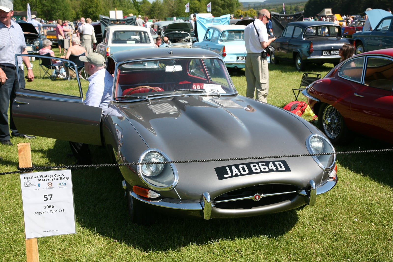 A silver Jaguar E-Type Series 1 2+2 coupe with covered headlamps at a show, front three-quarter view