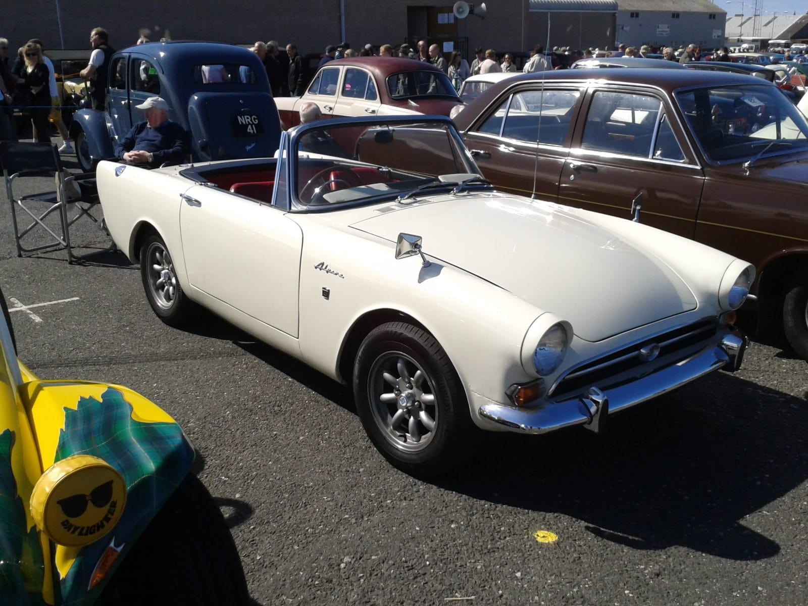 A cream Sunbeam Alpine Series V with the hood down at a busy classic car show