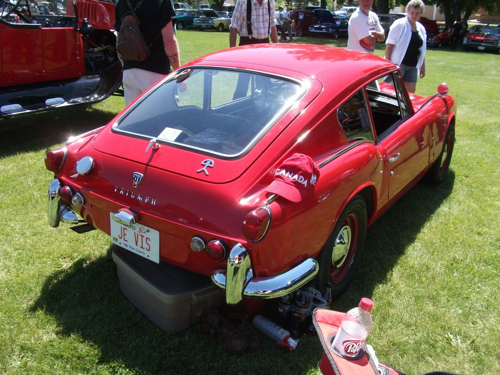 A red Triumph GT6 Mk1, rear three-quarter view showing the fastback roof, at a show