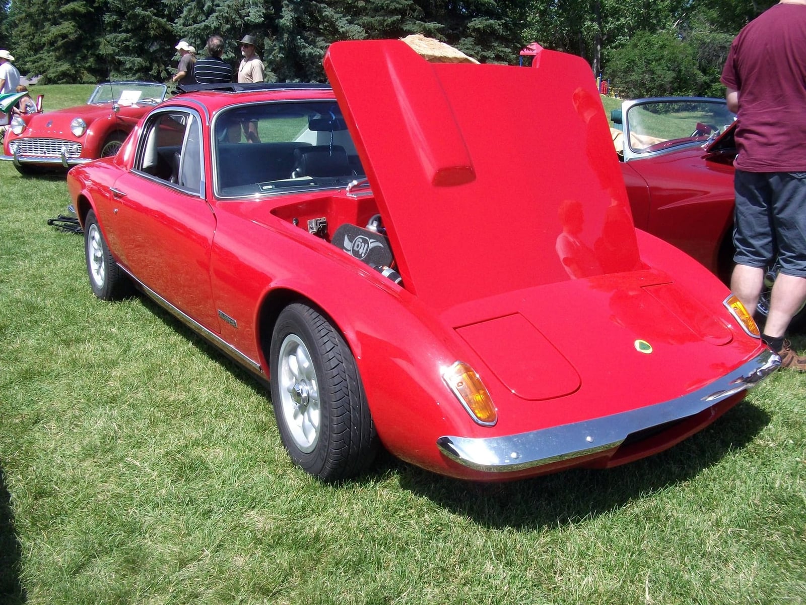 A red 1969 Lotus Elan Plus 2 with its bonnet raised at a classic car show