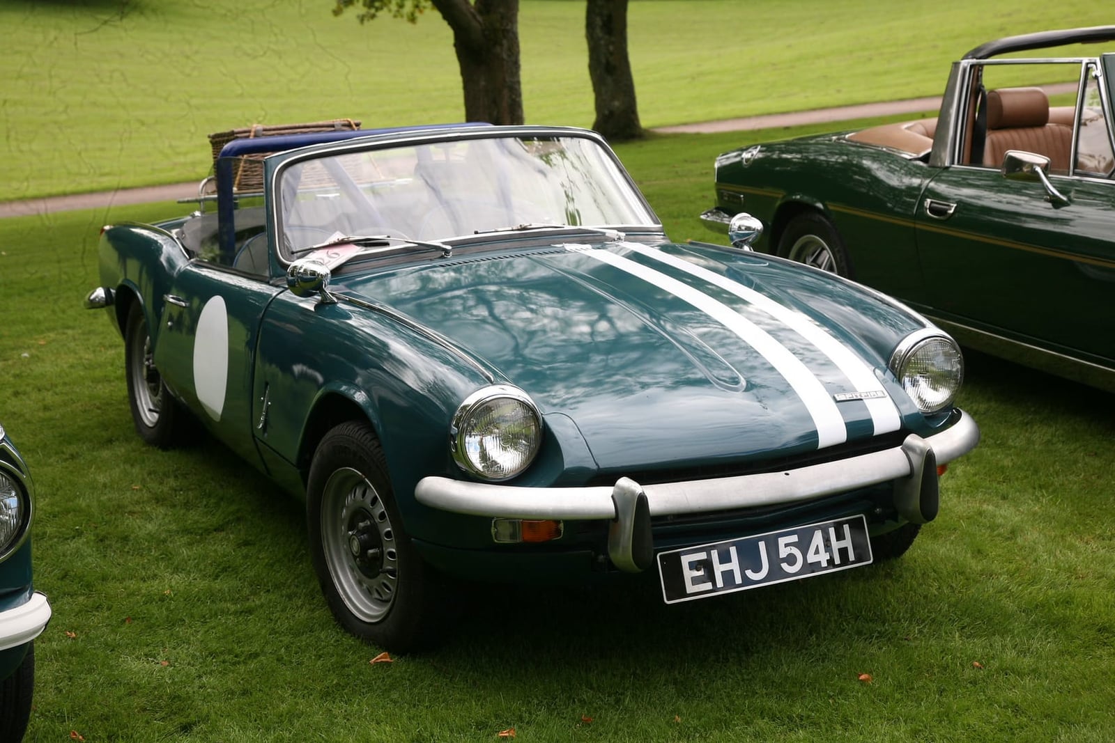 A dark green 1969 Triumph Spitfire Mk3 with white racing stripes and a UK registration on grass