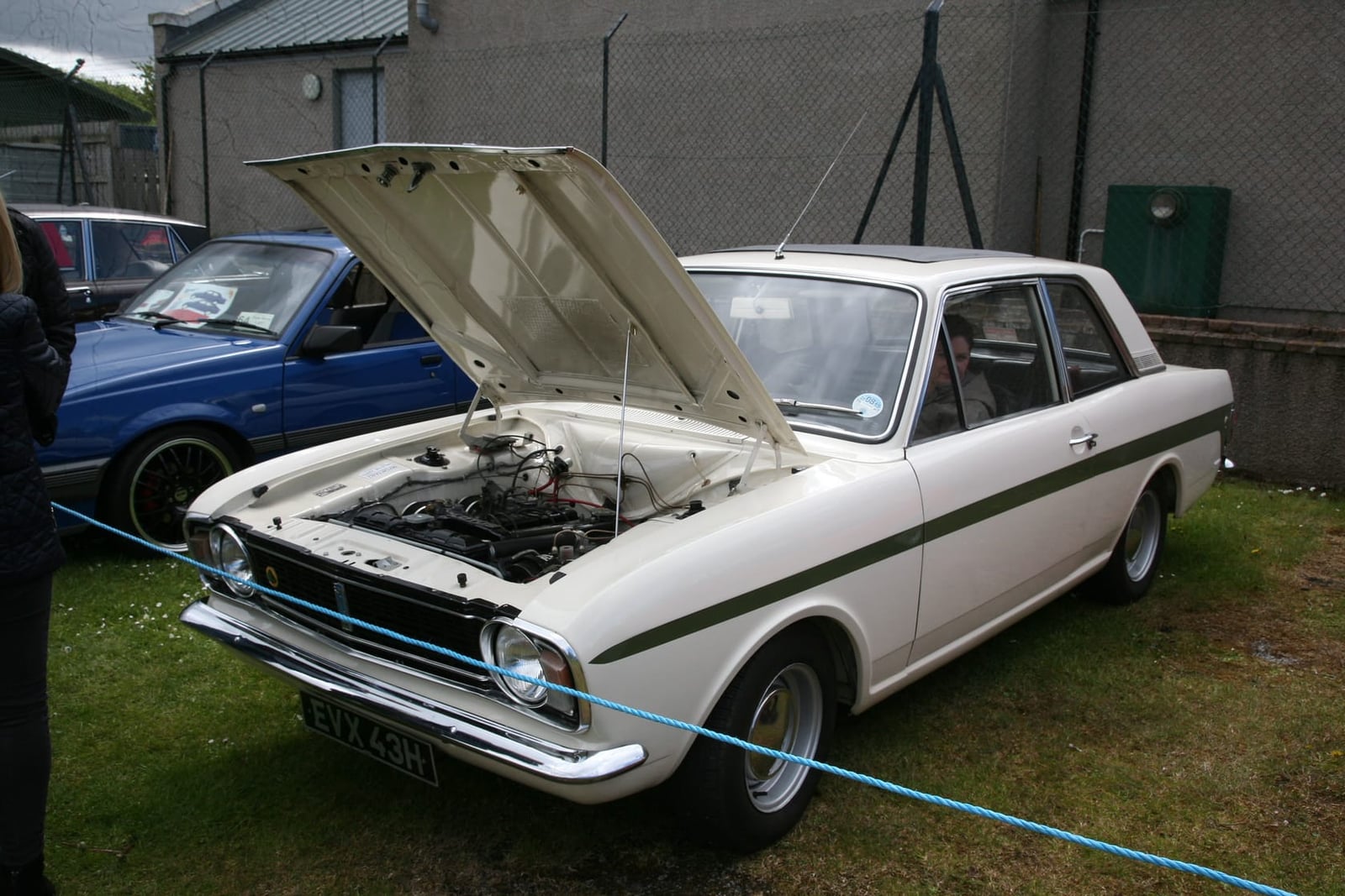 A white and green 1970 Ford Lotus Cortina Mk2 with its bonnet raised and a UK registration at a show