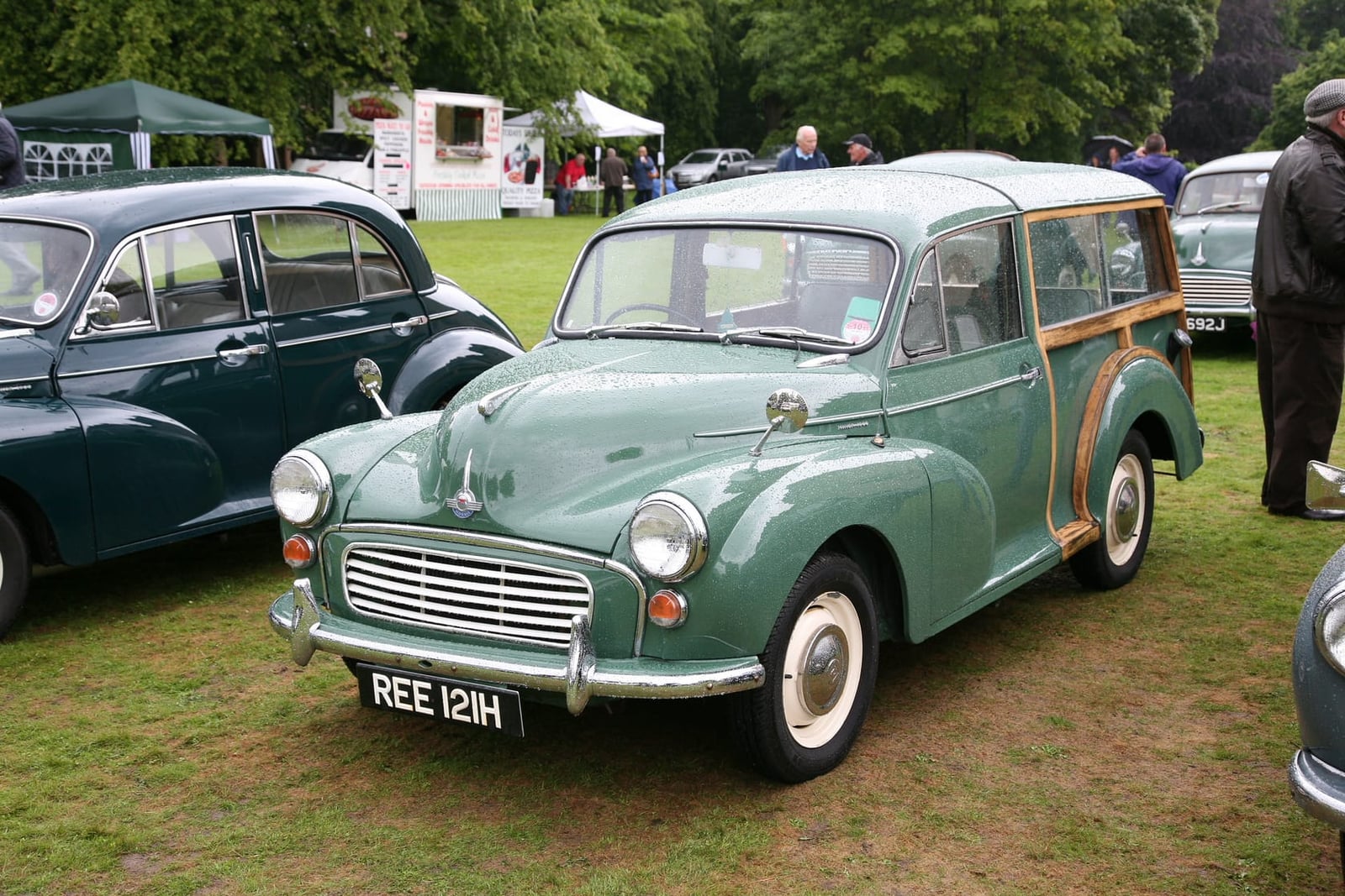 A green 1970 Morris Minor 1000 Traveller with wood-framed rear bodywork at a classic car show, UK registration REE 121H