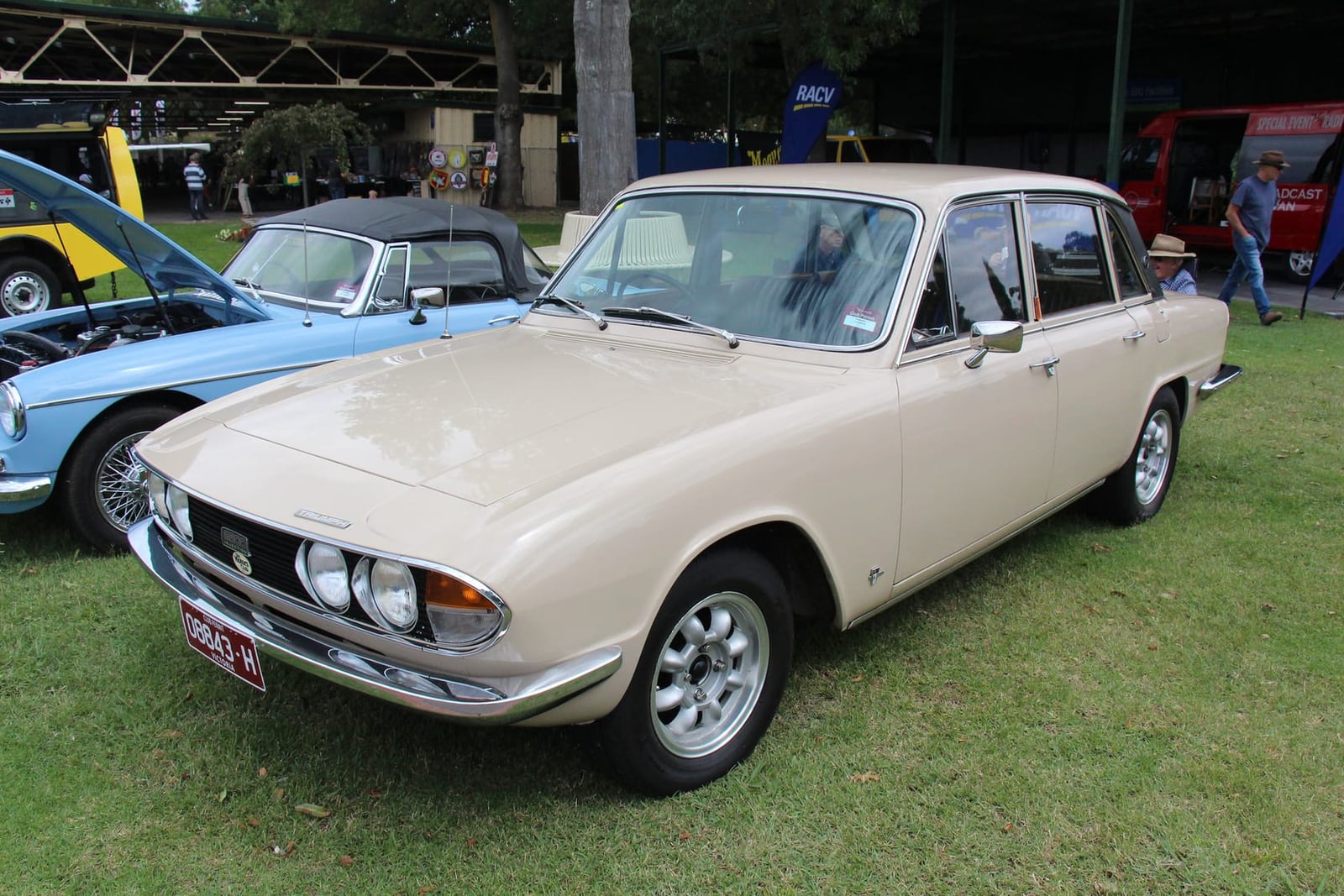 A cream 1970 Triumph 2500 Mk II PI saloon on grass at a classic car show, front three-quarter view