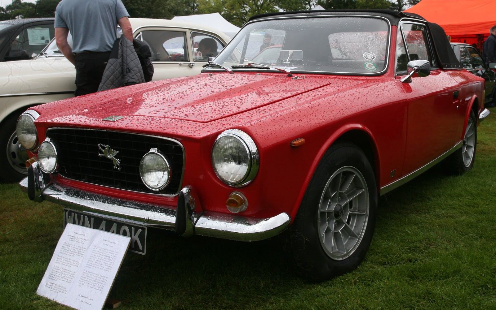 A red Gilbern Invader Mk II coupe on chrome wire wheels, front three-quarter view at a classic car show