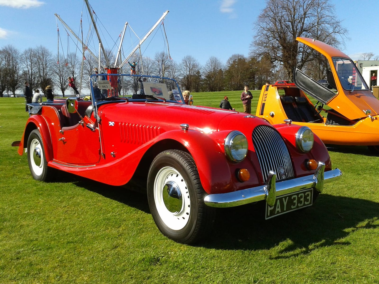 A red 1972 Morgan 4/4 two-seater on grass at a classic car show, front three-quarter view, UK registration AY 333