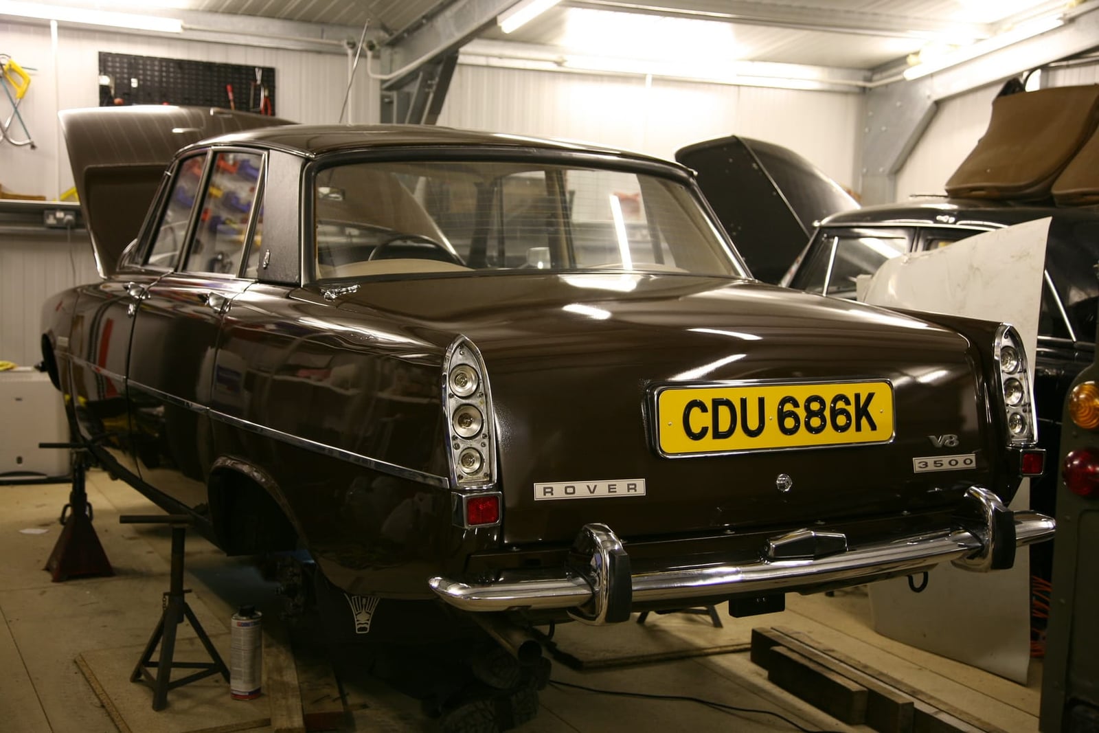 A brown Rover P6 3500 in a workshop with its rear panels and boot lid removed, exposing the structure beneath
