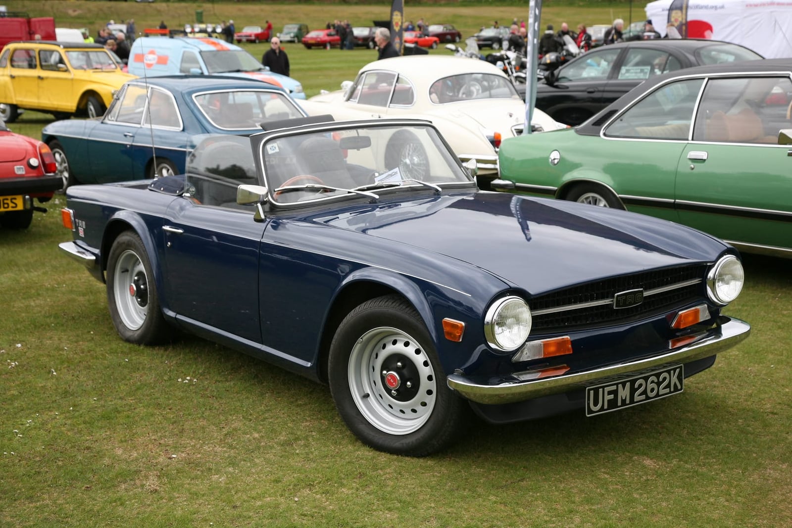 A dark blue 1972 Triumph TR6 on steel wheels with a UK registration, in unrestored condition at a show
