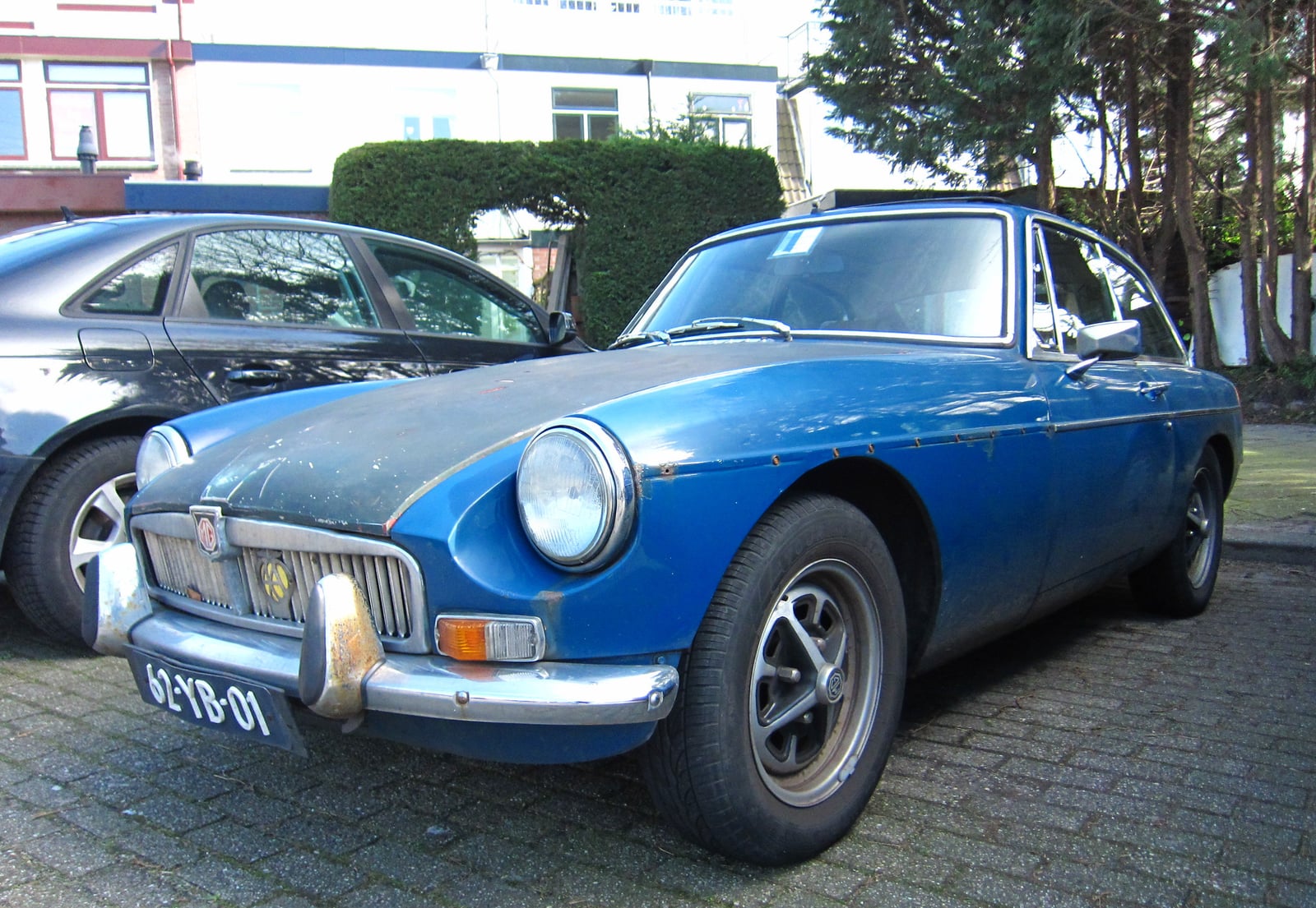 A blue-green MG MGB GT, front three-quarter view on a driveway