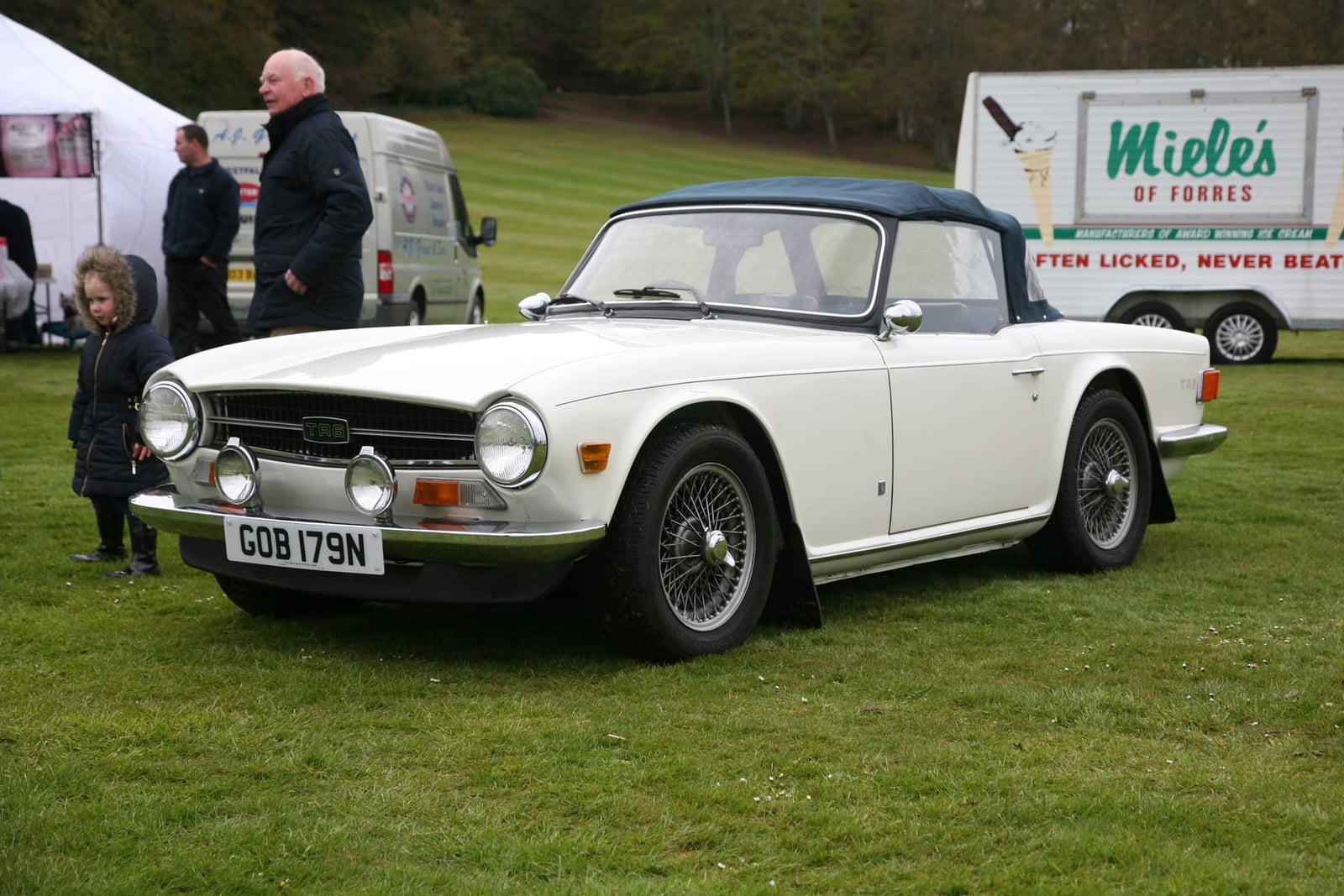 A white 1974 Triumph TR6 fitted with the factory hardtop, UK registration, on a show field in Scotland