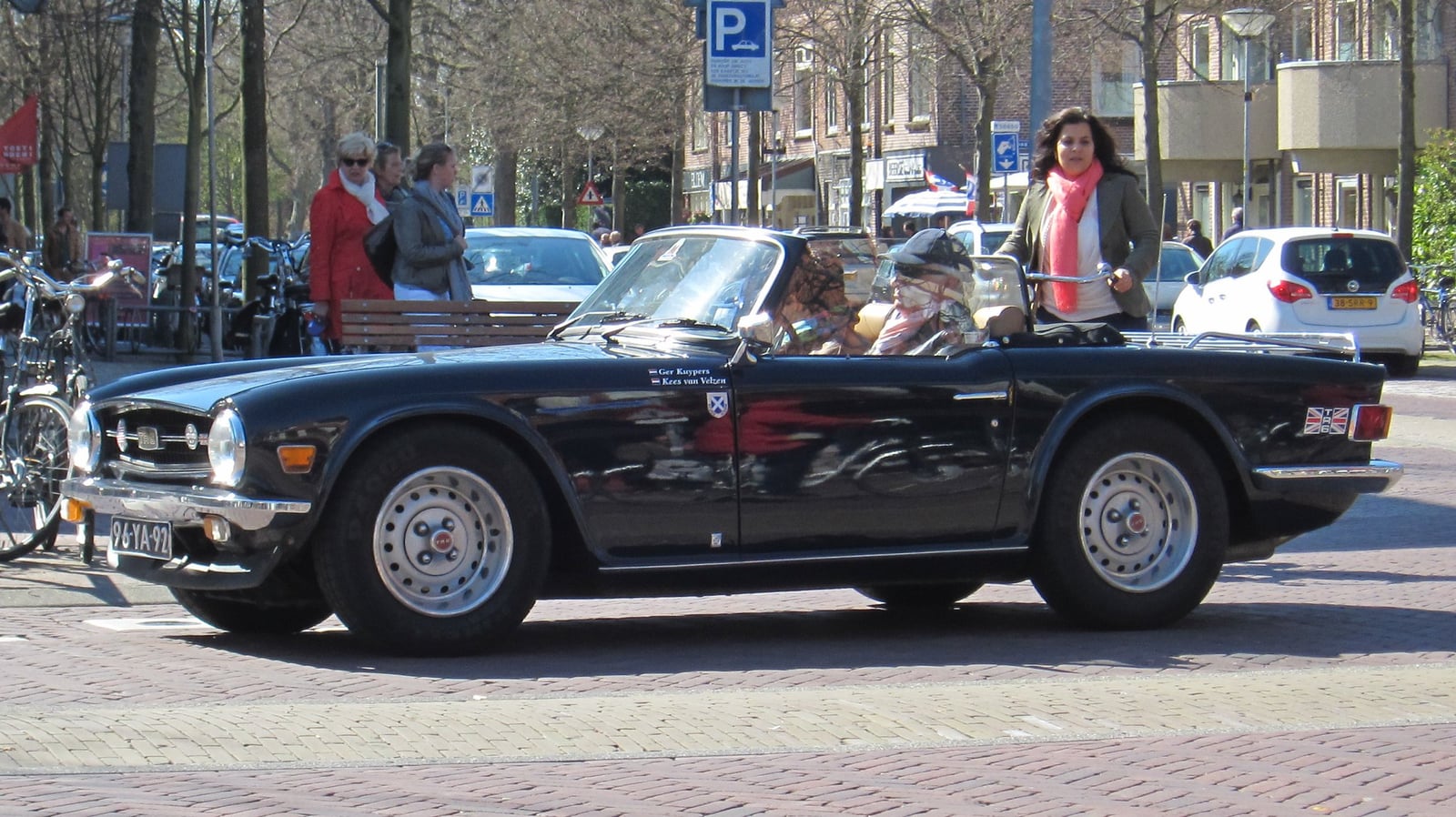 A black Triumph TR6 being driven through a town square with the top down