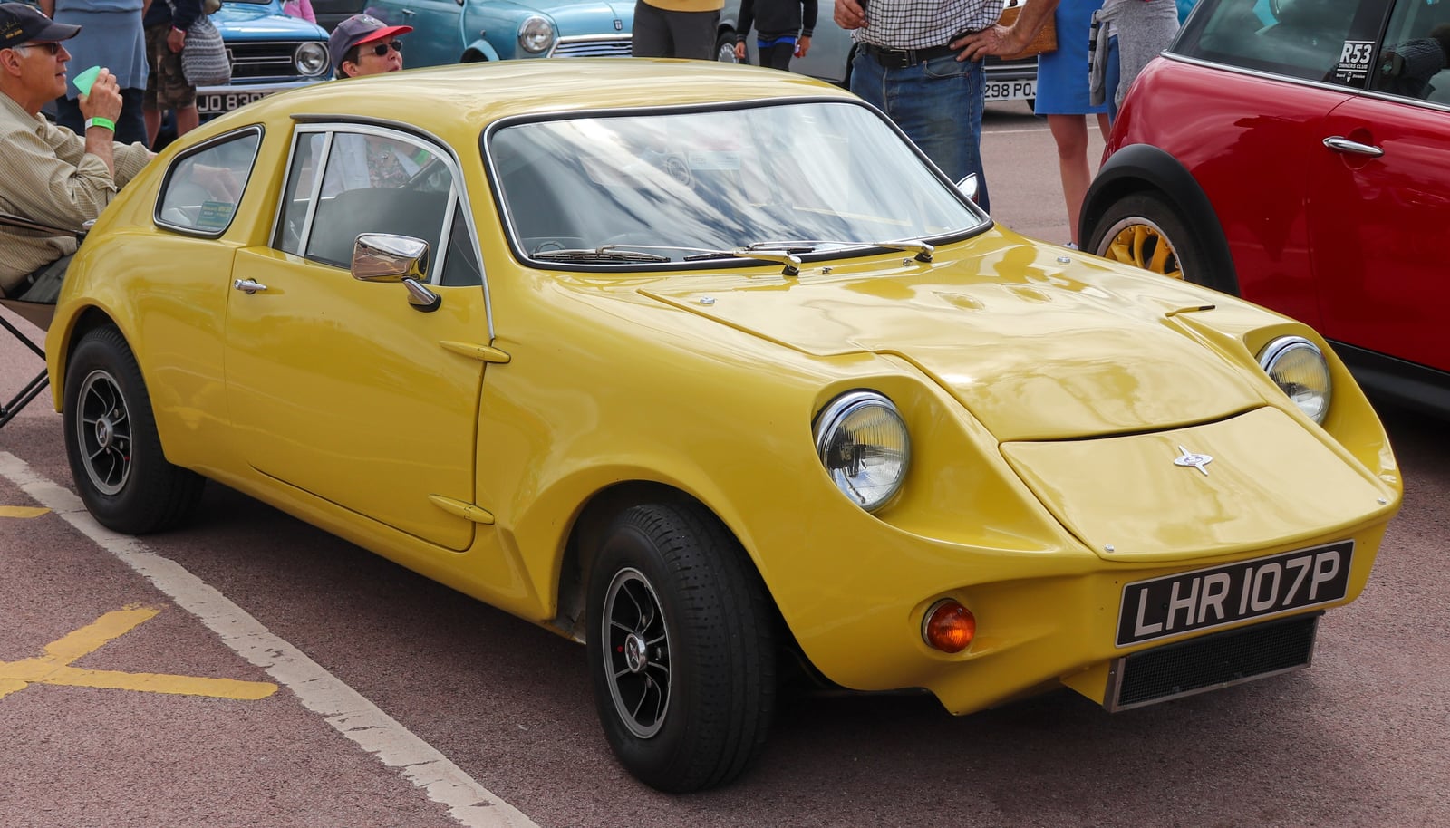 A yellow 1975 Mini Marcos 850cc coupe, front three-quarter view at a classic car show