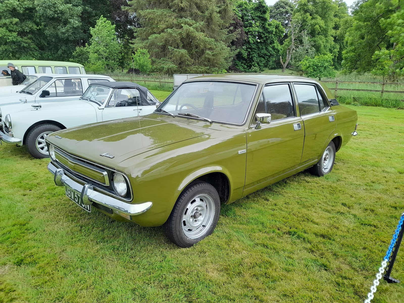 An olive-green Morris Marina four-door saloon, front three-quarter view, on grass at a show