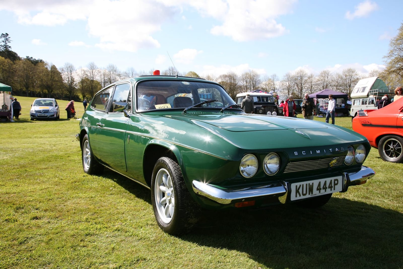 A green 1975 Reliant Scimitar GTE SE5a on grass at a classic car show, front three-quarter view, UK registration KUW 444P