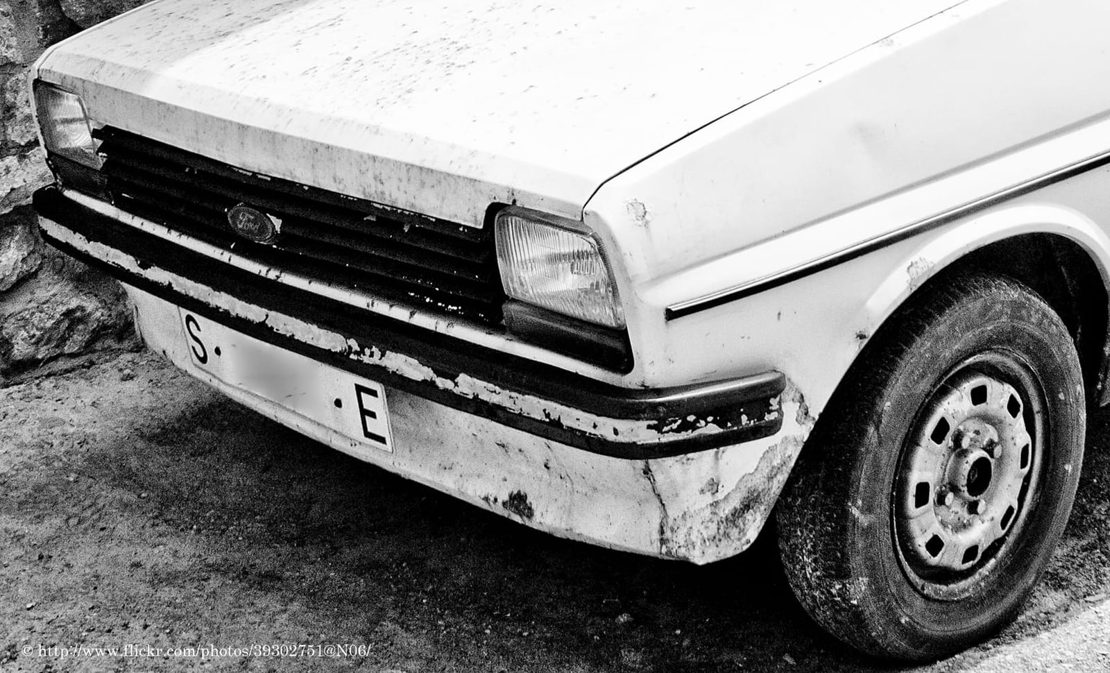 A black and white close-up of a rusted Ford Fiesta Mk1 front wing, bumper and headlamp
