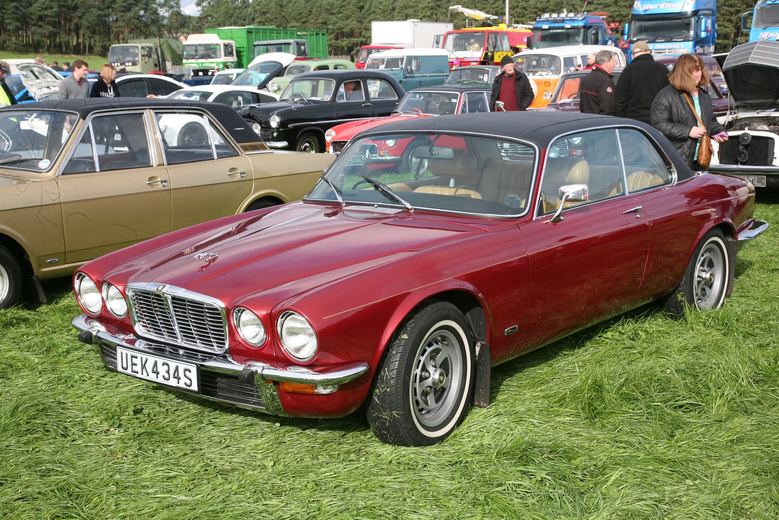 A red Jaguar XJ12 two-door coupe on grass at a show, front three-quarter view