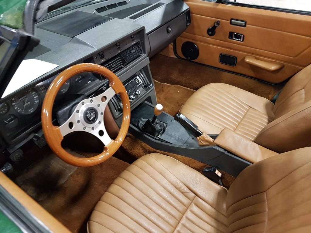 The tan cloth and vinyl interior of a 1980 Triumph TR7 showing the dashboard, centre console and a wood-rimmed steering wheel