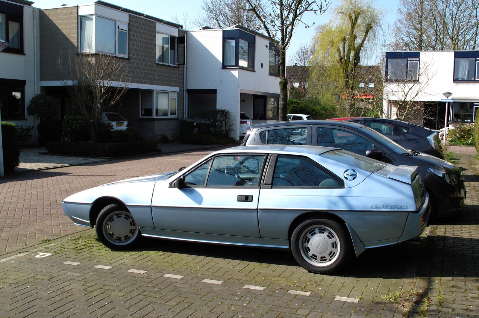 A silver 1986 Lotus Excel 2.2 SV in profile on a residential street
