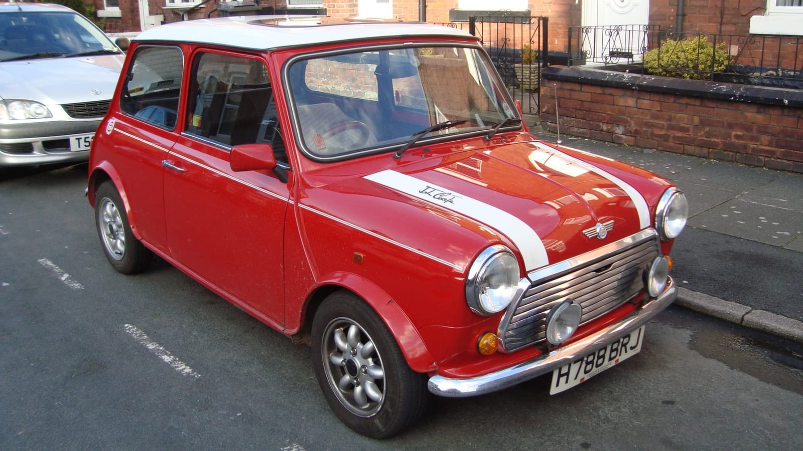A red 1990 Rover Mini Cooper with a white roof and bonnet stripes and a UK registration, parked at the kerb