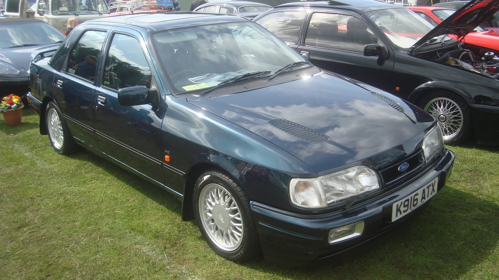 A dark green Ford Sierra Sapphire RS Cosworth 4x4 with a UK registration parked among other cars