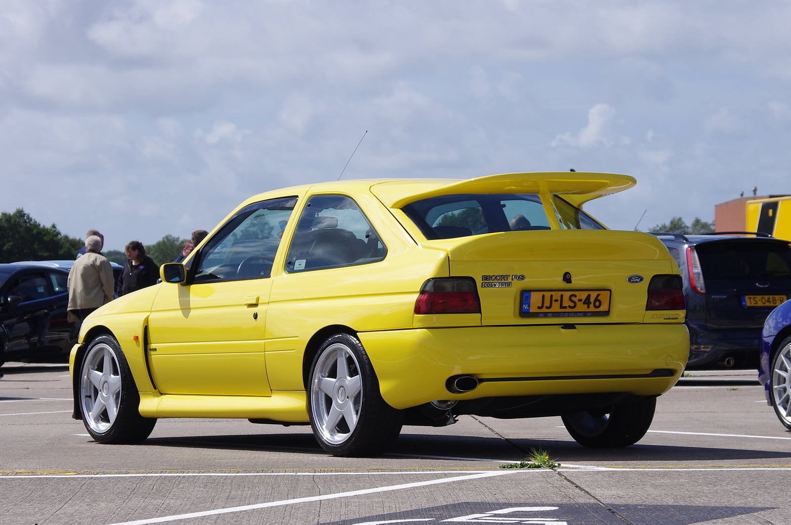 A yellow Ford Escort RS Cosworth, rear three-quarter view showing the large twin-plane whale-tail rear wing