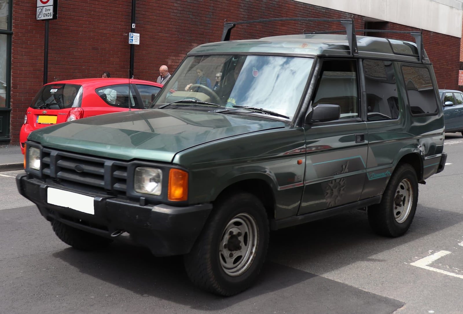 A green 1994 Land Rover Discovery 1 three-door with a roof rack parked in a city street