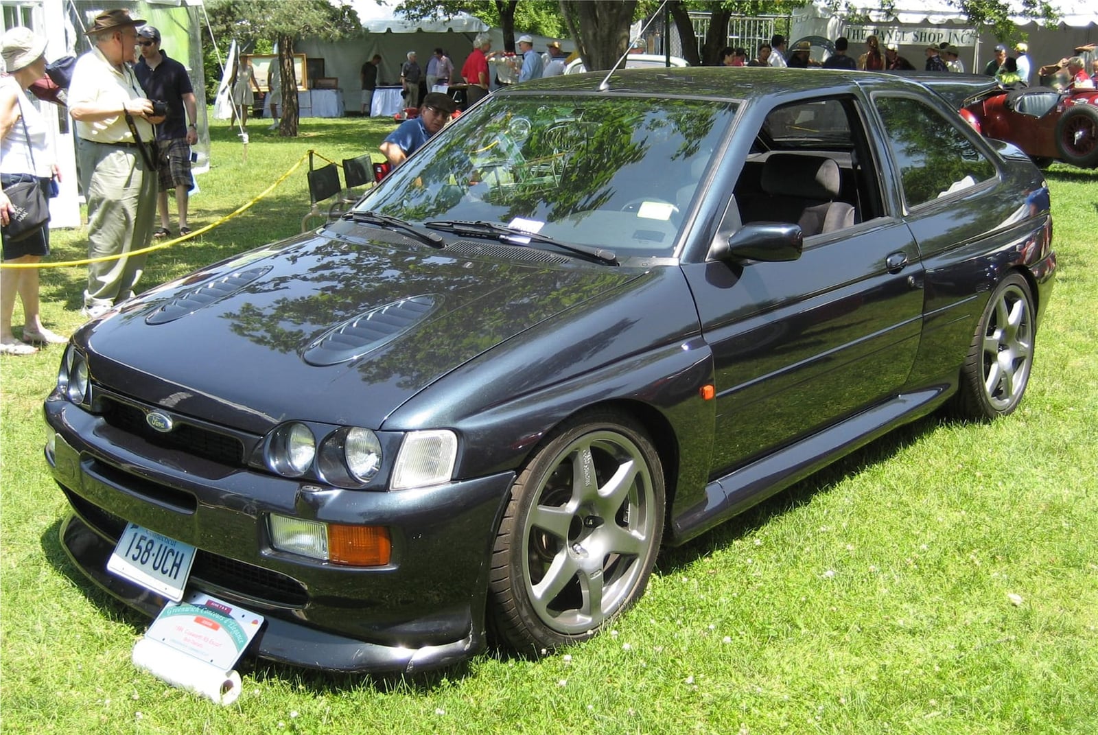 A dark grey 1996 Ford Escort RS Cosworth on grass at a classic car show, front three-quarter view