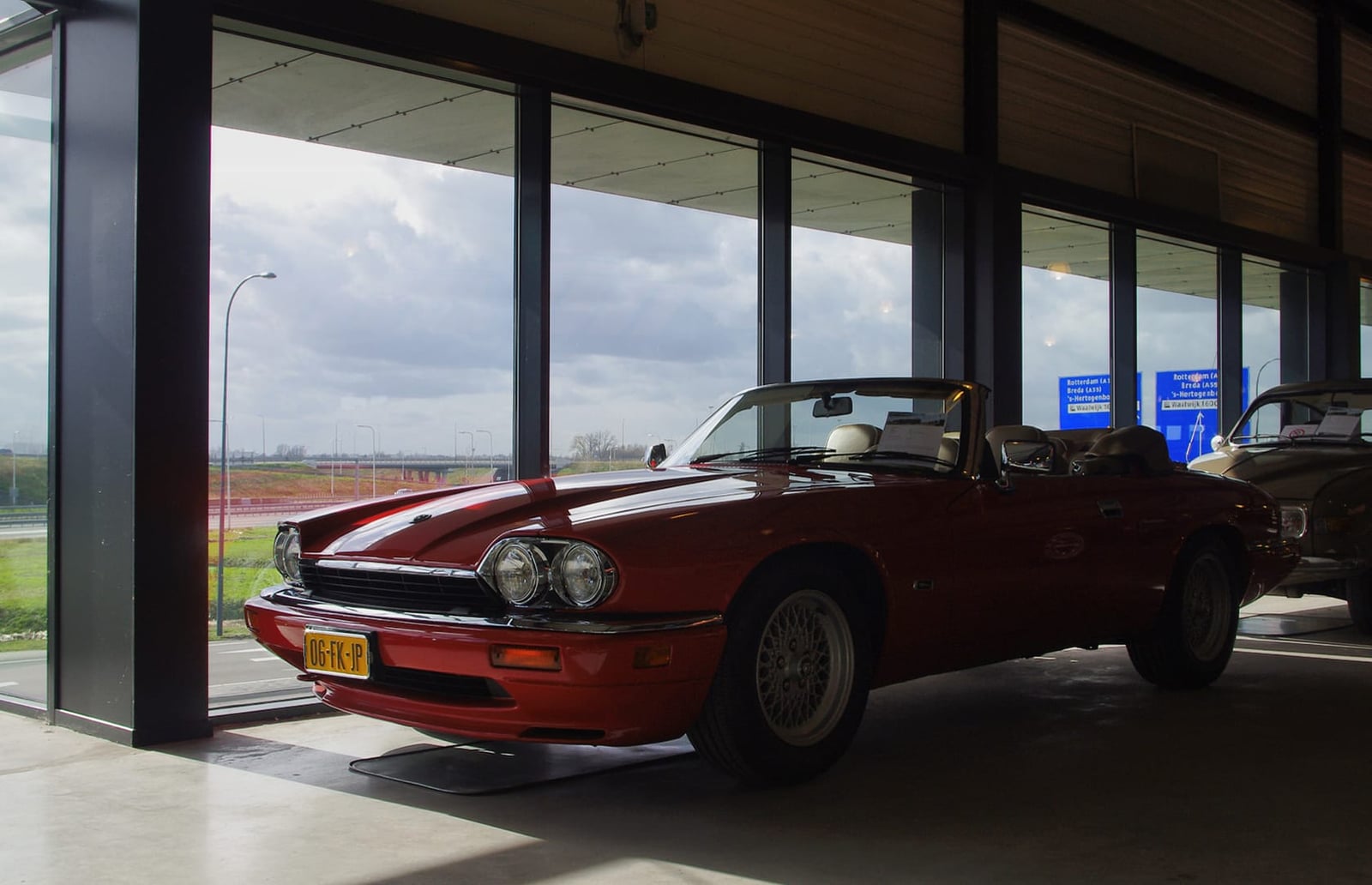 A red 1996 Jaguar XJS 4.0 Celebration convertible displayed indoors at a dealership with its hood down