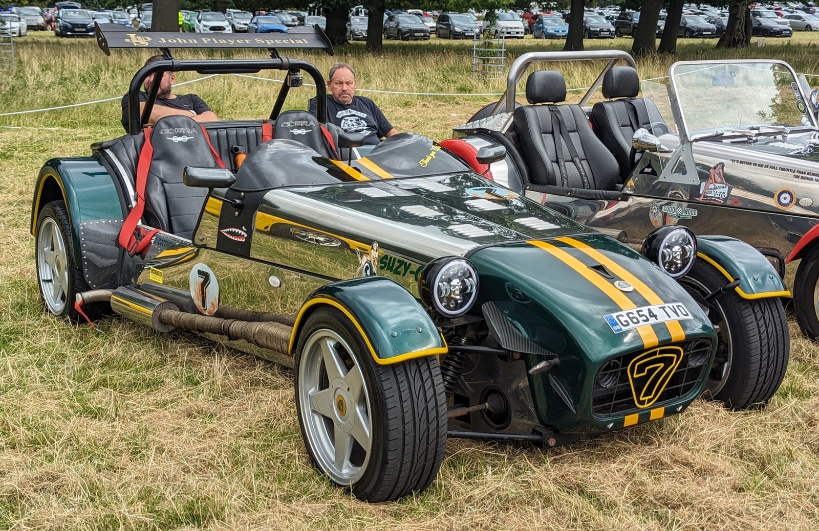 A green and black Robin Hood 2B Seven-style roadster with occupants, three-quarter front view on grass at a show