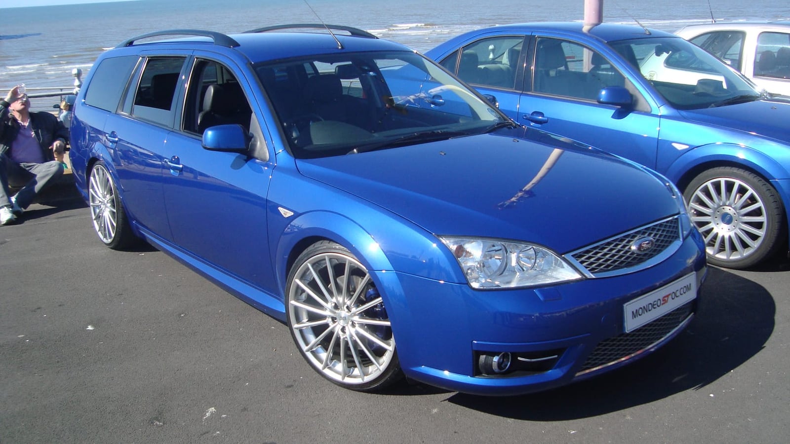 A 2006 Ford Mondeo ST220 estate in Performance Blue on a seafront at a show, another ST220 behind