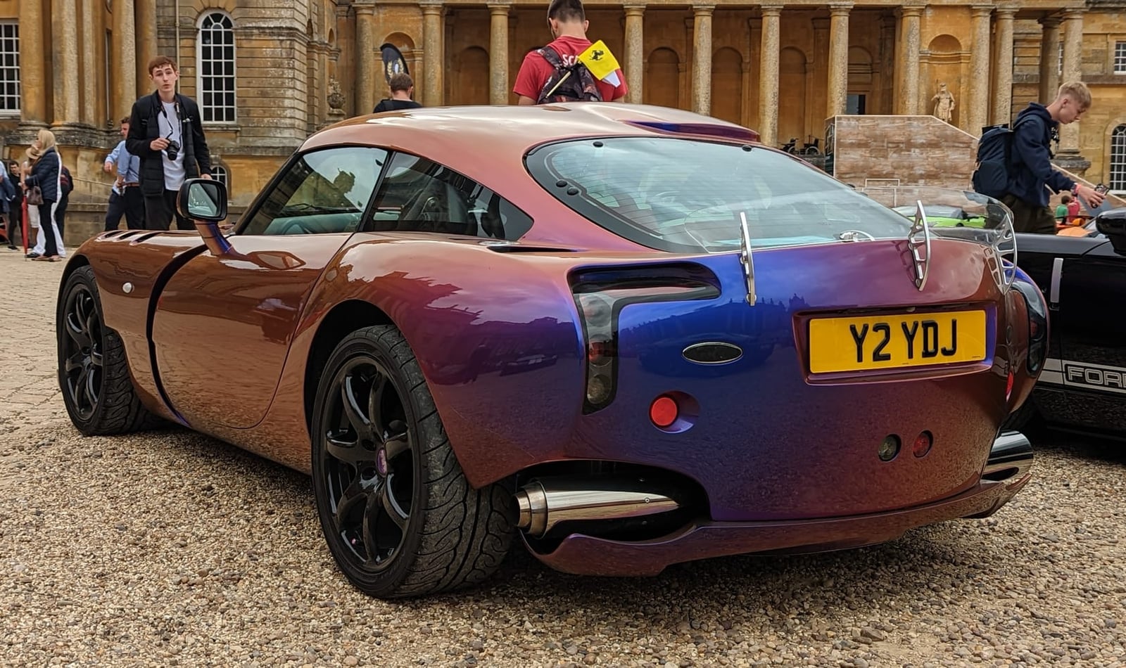 The rear of a 2006 TVR Sagaris in colour-shift paint with a UK registration, parked on gravel outside a stately home