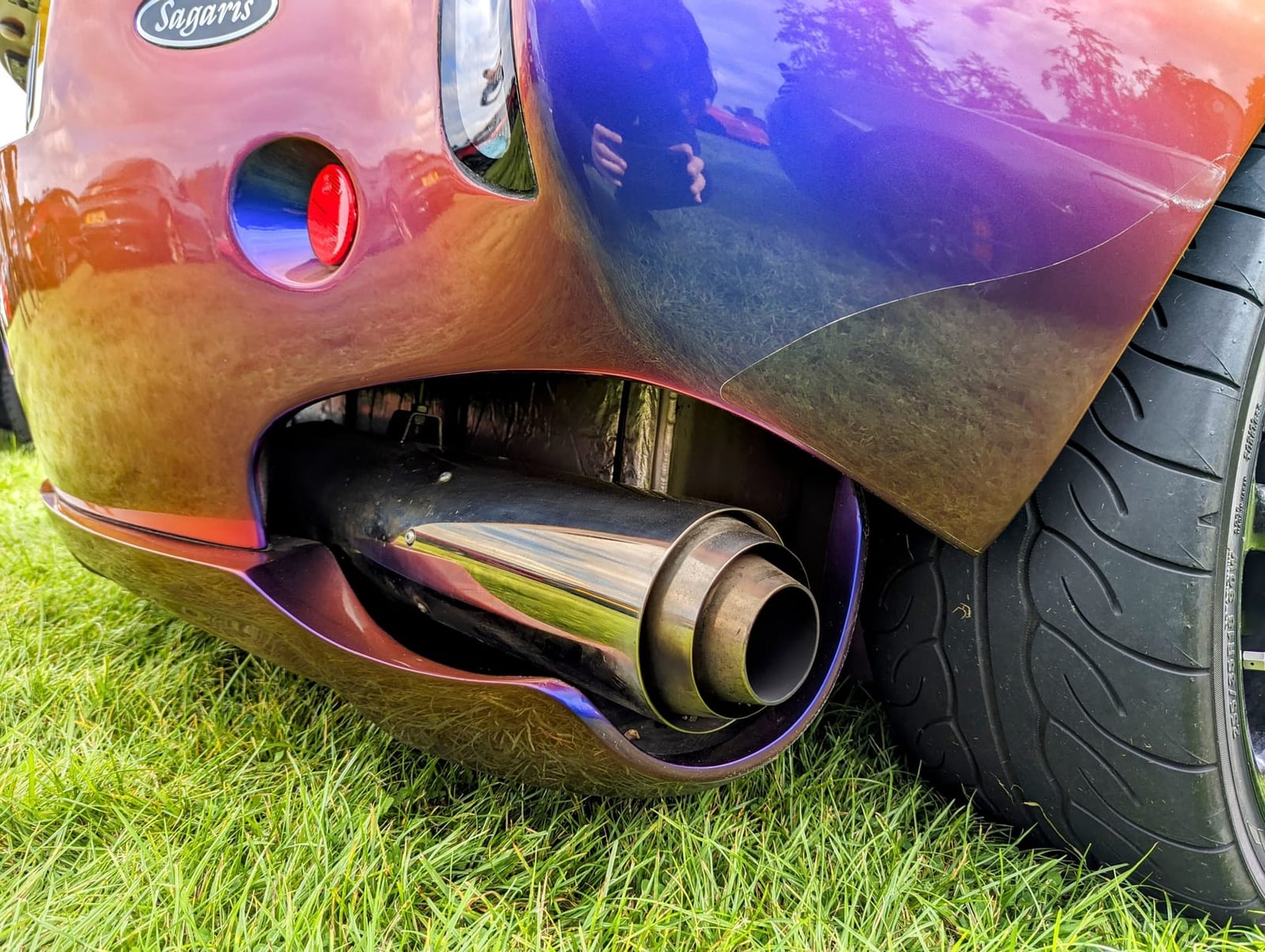 Close-up of the side-exit exhaust of a TVR Sagaris in colour-shift paint, the tailpipe emerging in front of the rear wheel