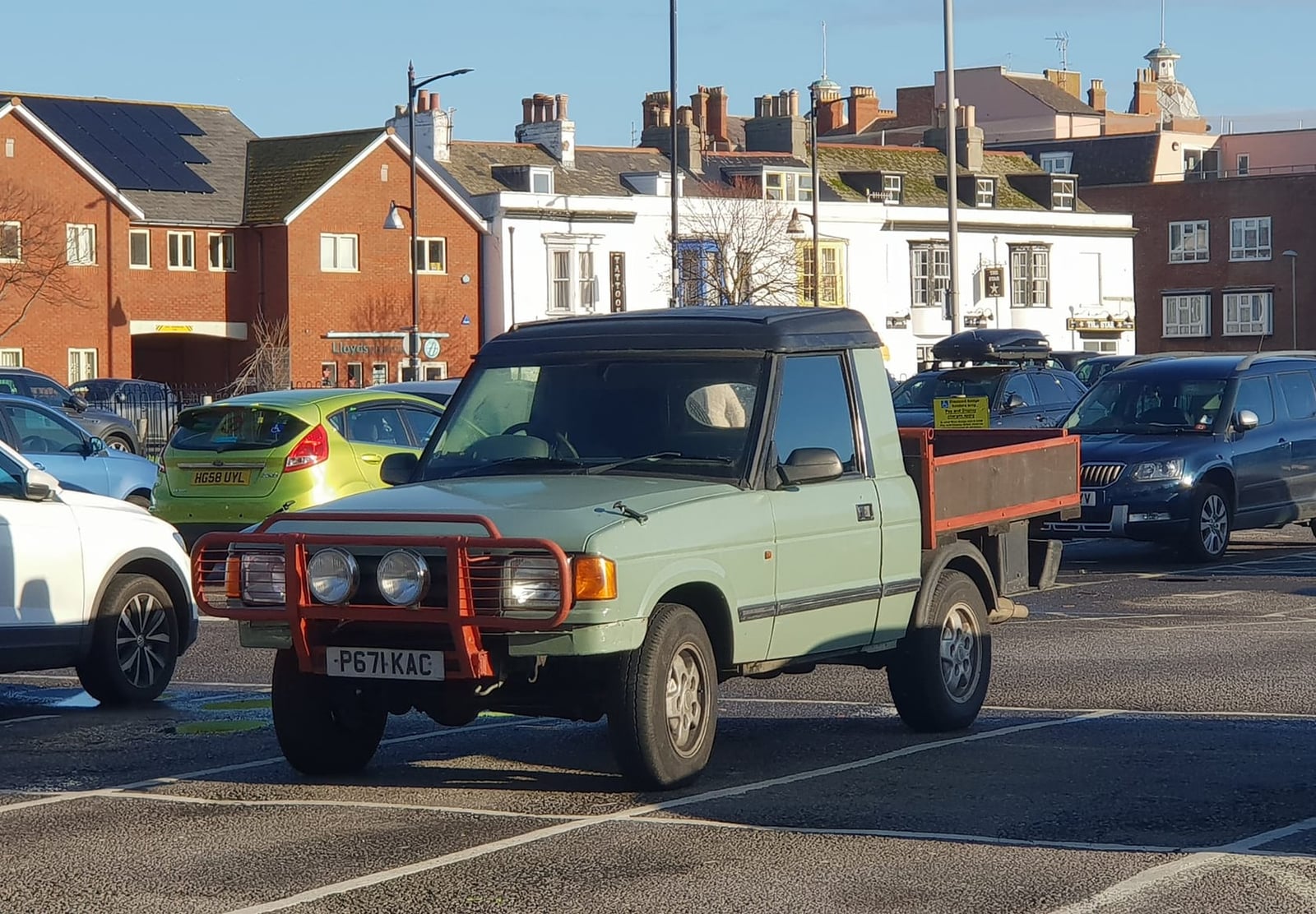A pale green Land Rover Discovery 1 converted into a flat-bed pickup, parked in a street car park