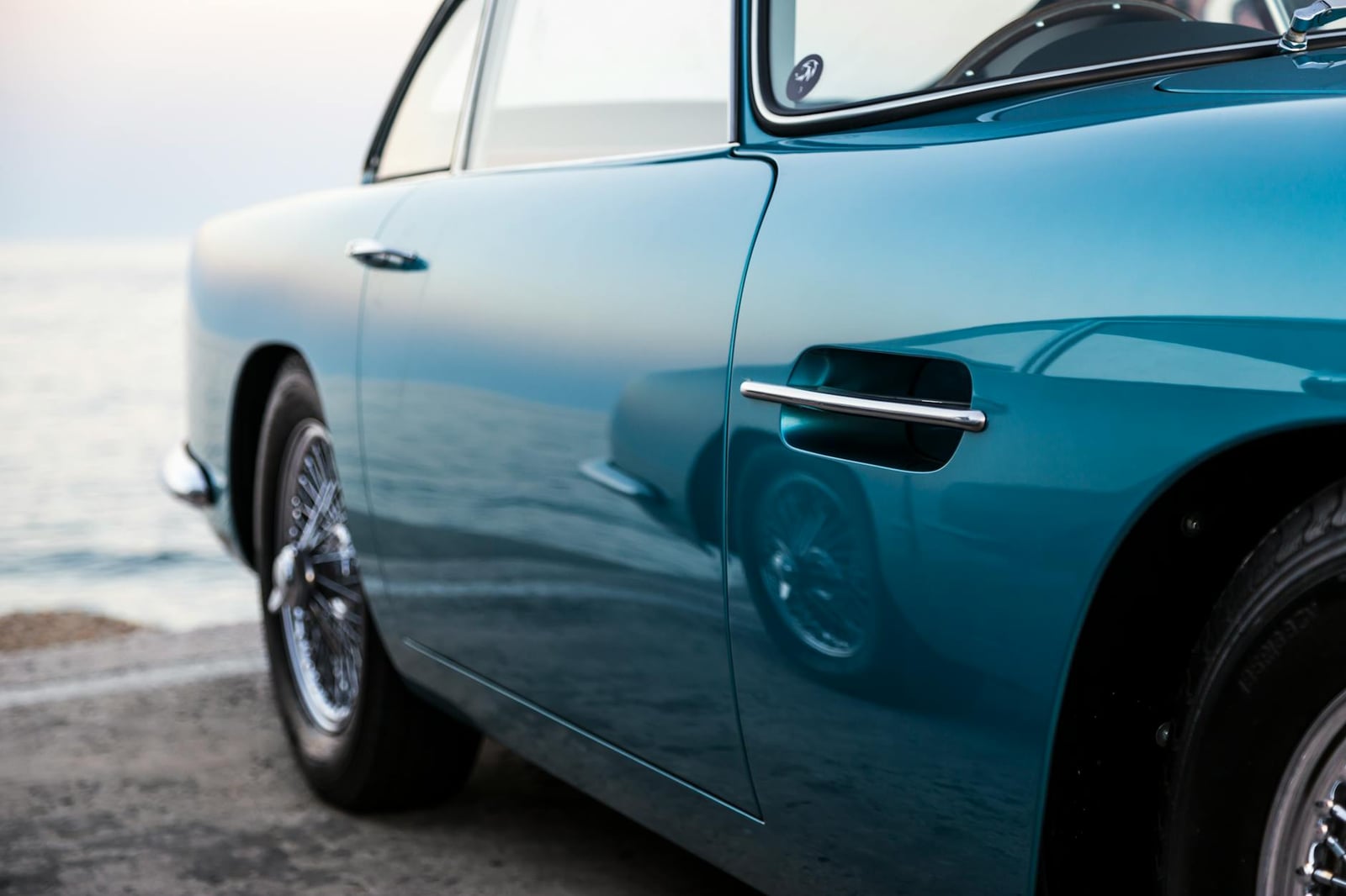 A blue Aston Martin DB5 parked near the sea, front three-quarter view